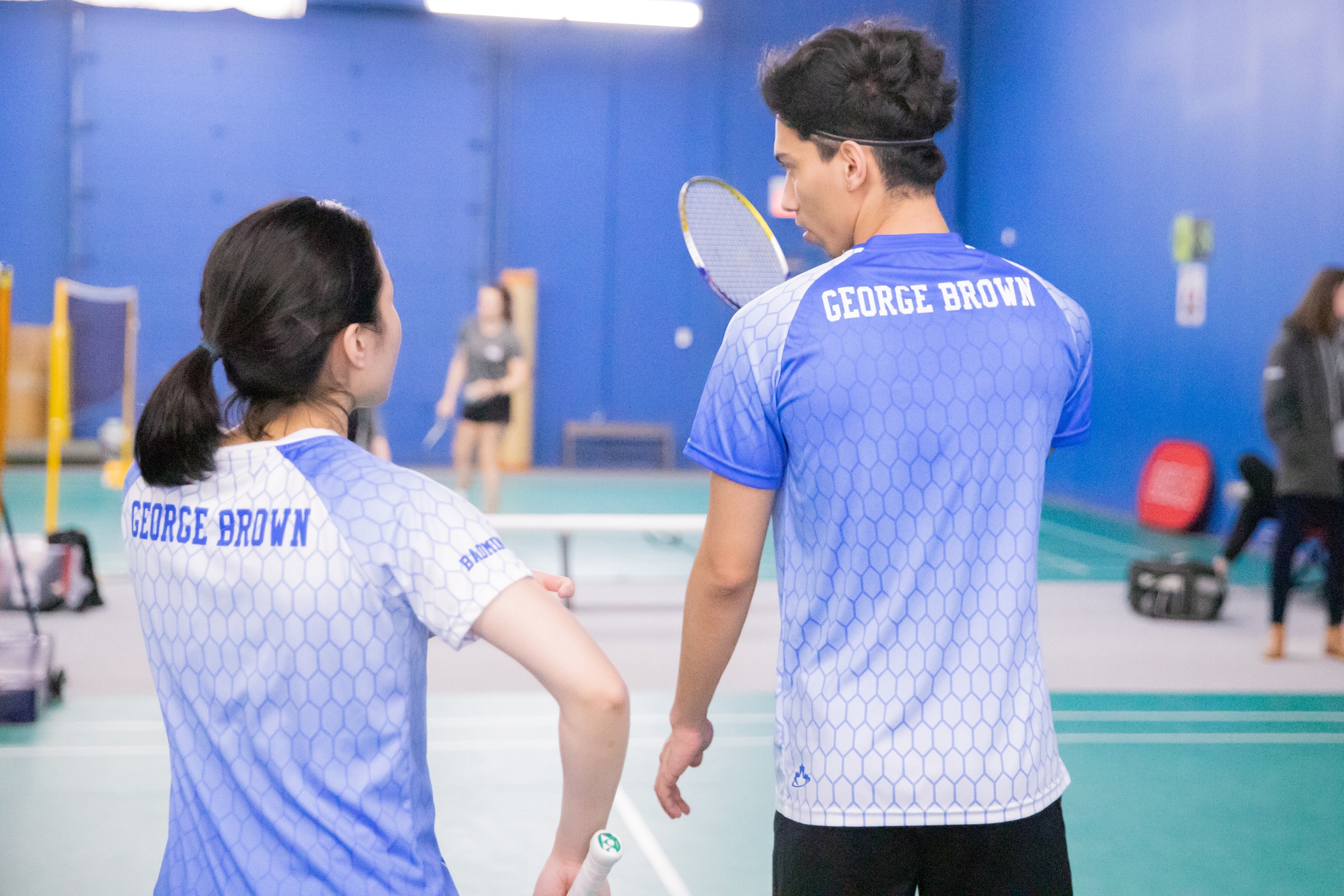 two badminton players talk to each other, viewed from behind
