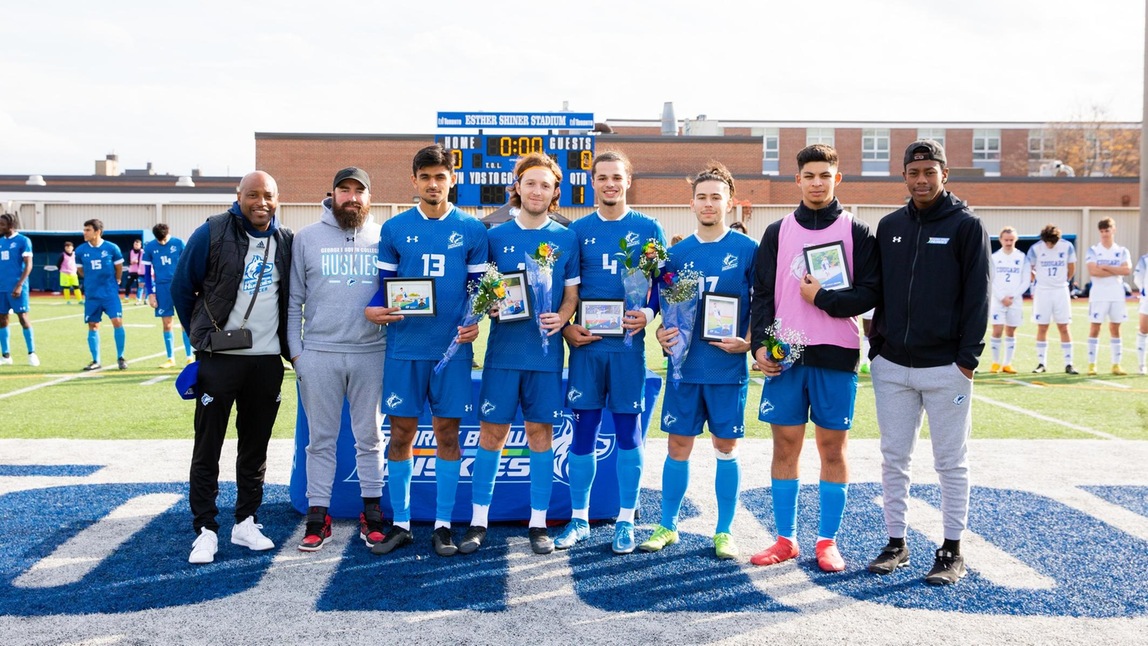 Mens soccer graduating athletes with coaches. Players lined up holding flowers and framed photos.
