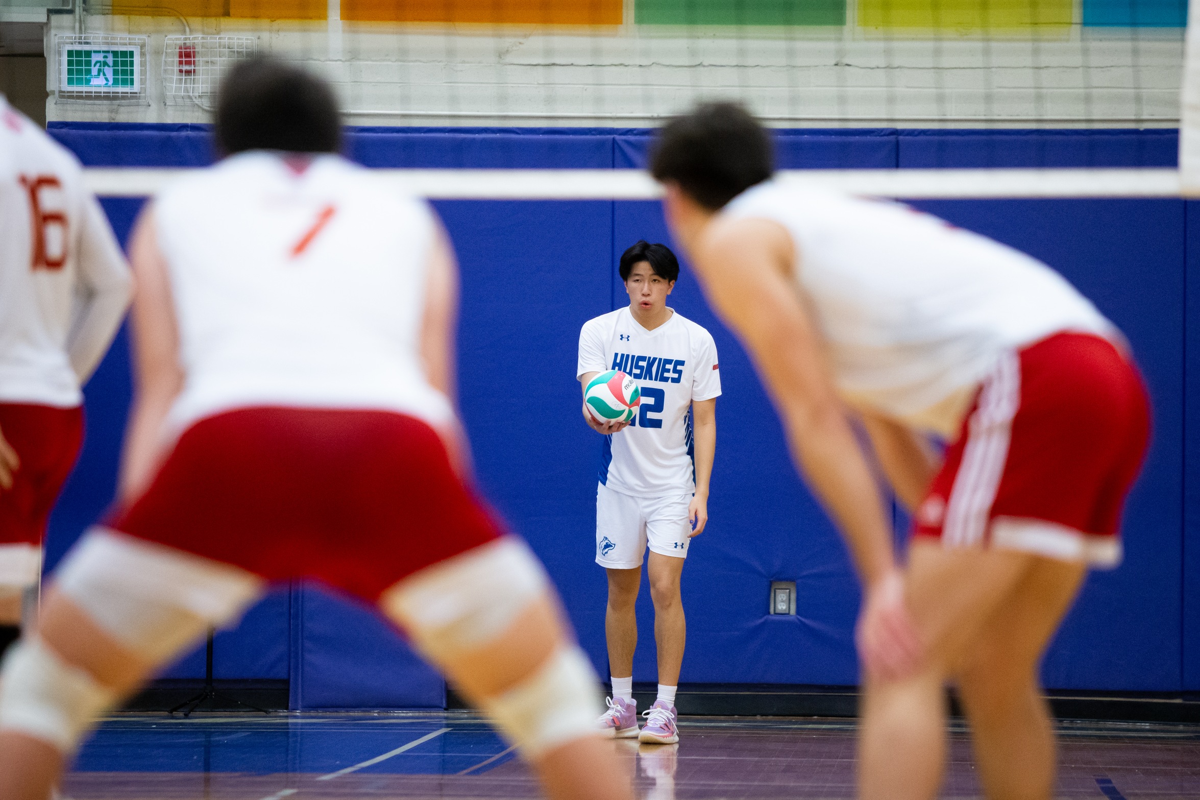 Huskies players waits to serve ball in the distance, between two defensive players at the net